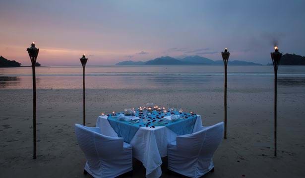 private dining table set up on the beach  decorated in roses and candles with a view of the datai bay