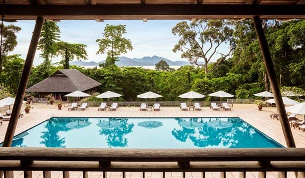wide shot of main pool area surrounded by sun chairs and umbrellas with datai bay in the background