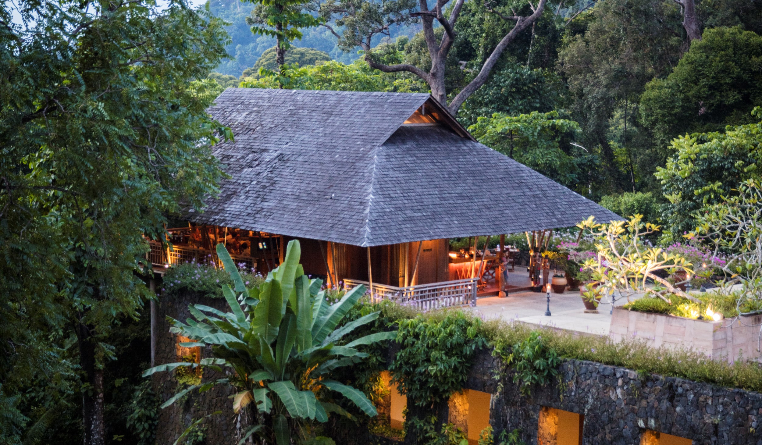 exterior shot of the a lit up pavilion restaurant in the evening surrounded by green rainforest