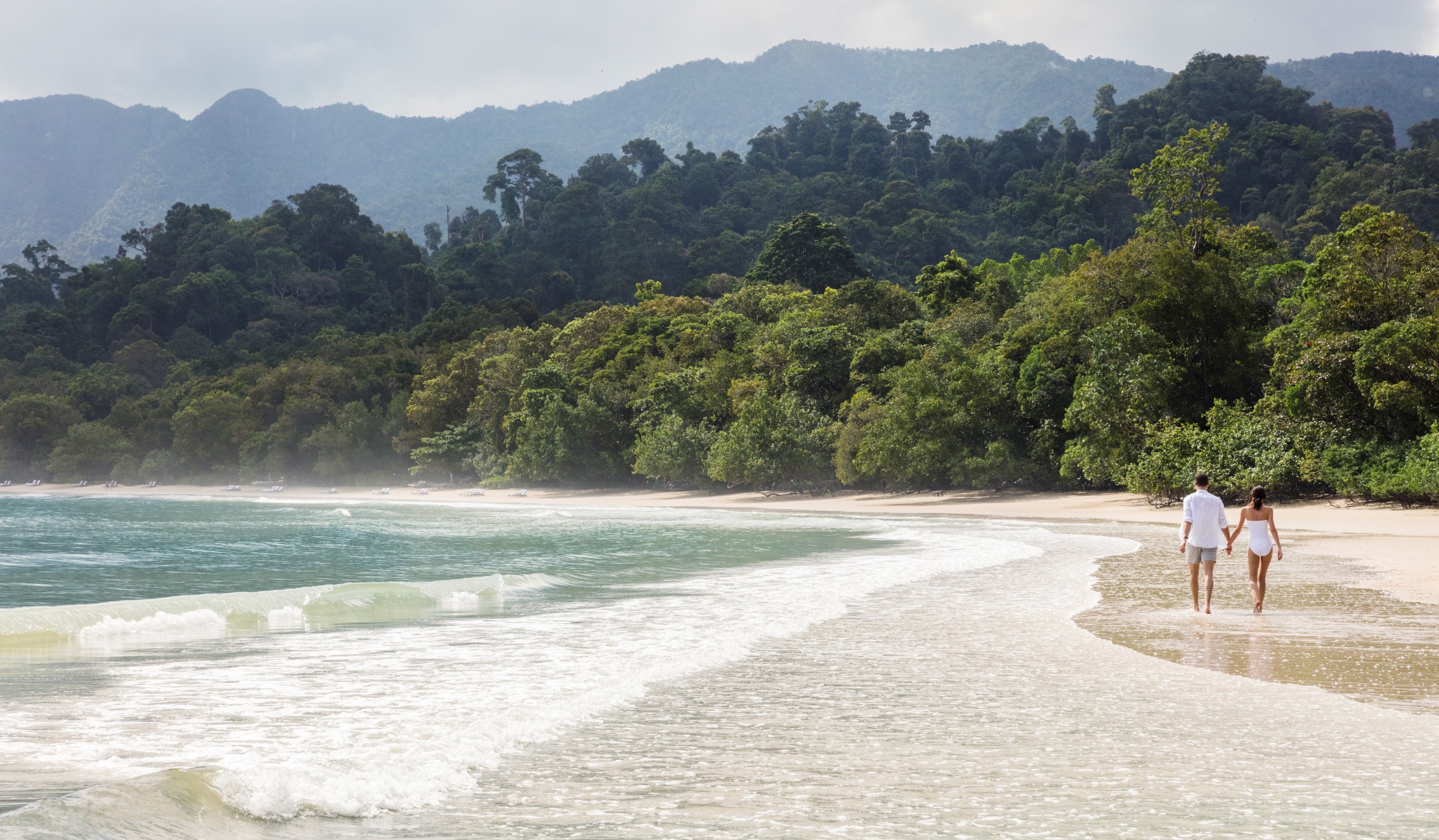 couple walking on a sunny beach with the waves coming in 