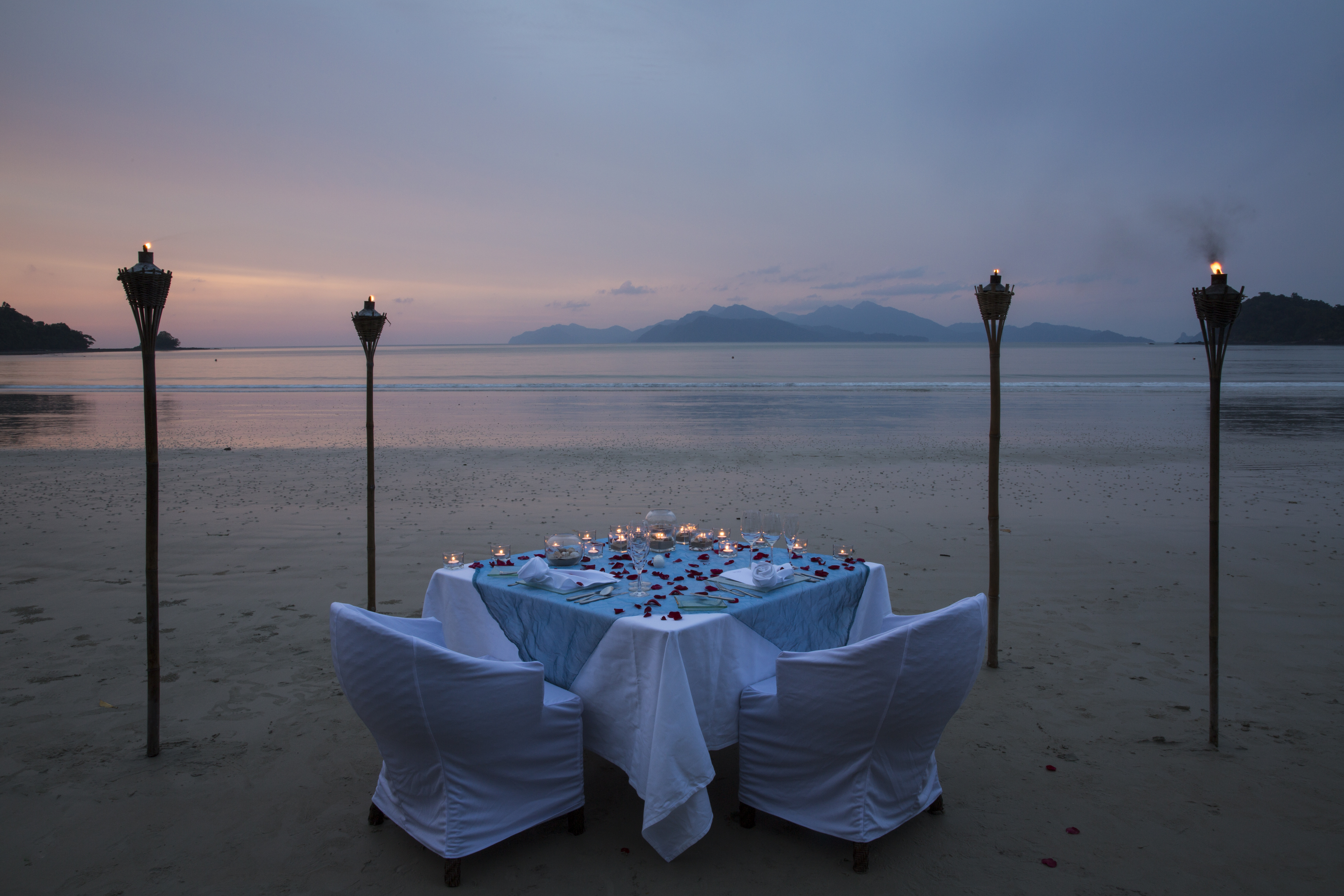 private dining table set up on the beach  decorated in roses and candles with a view of the datai bay