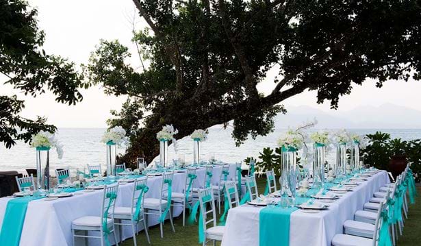 Two long blue and white tables equipped with chairs  and decorated with flowers in tall glasses overlooking the datai bay