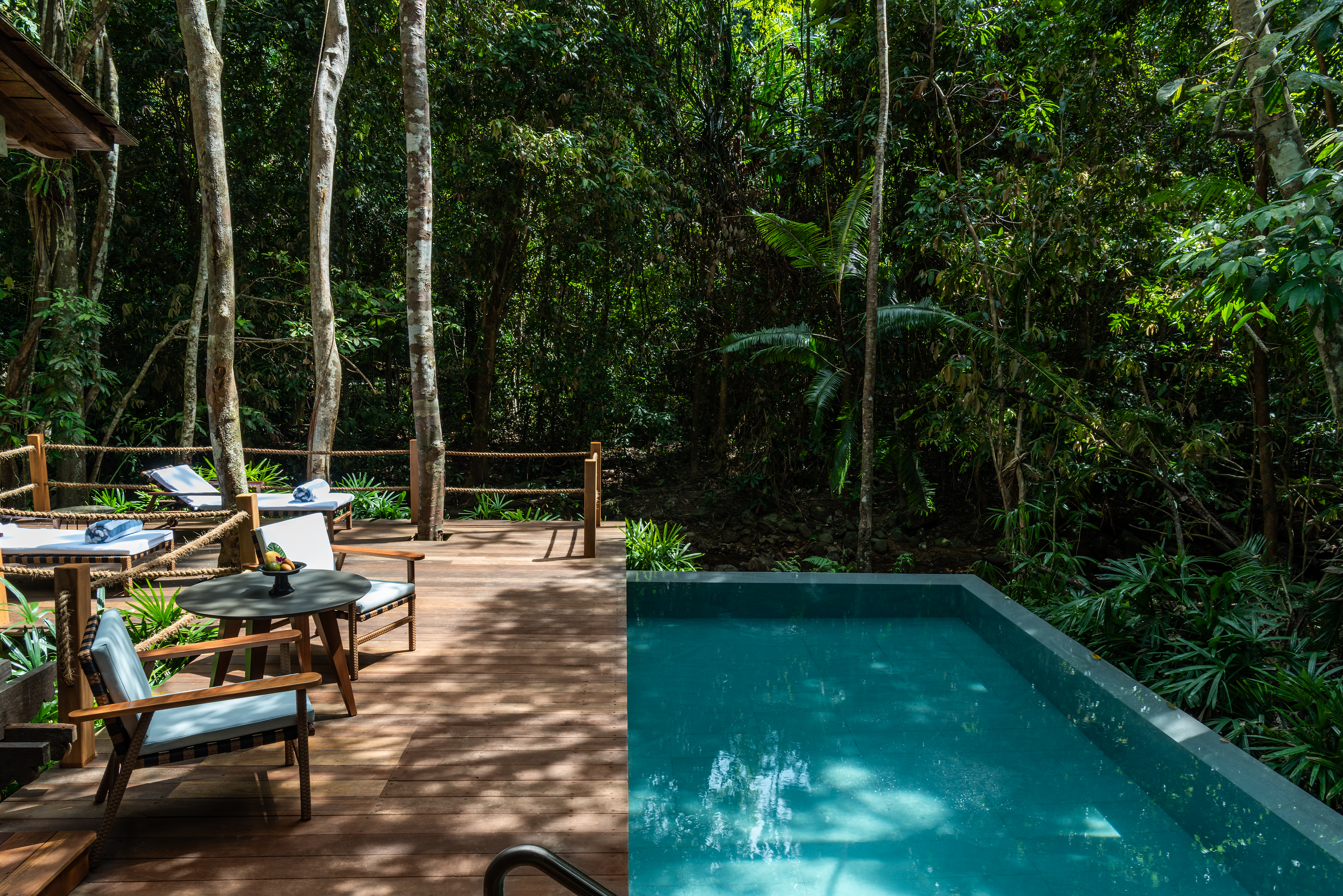 a pool patio with comfy chairs and a table Infront of a private pool at a rainforest pool villa