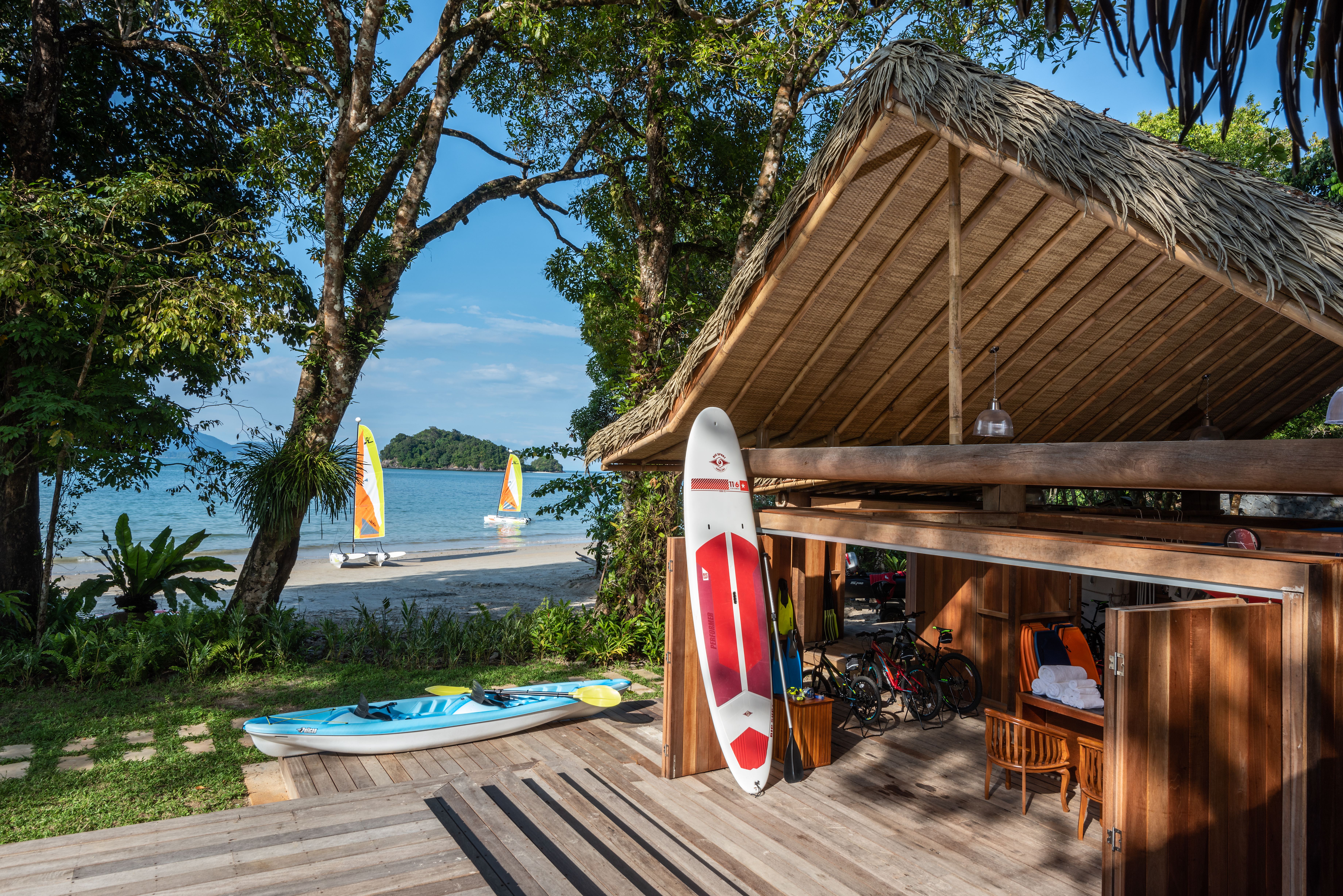 water sports centre equipped with surfing boards, bikes and an inflatable canoe with people sailing in the background