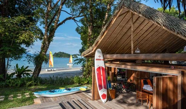 water sports centre equipped with surfing boards, bikes and an inflatable canoe with people sailing in the background