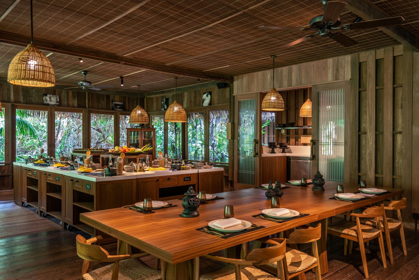 interior shot of cooking class room equipped with a full dining table and chairs and a kitchen with various foods and kitchen utensils on it 