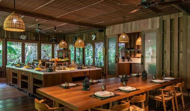 interior shot of cooking class room equipped with a full dining table and chairs and a kitchen with various foods and kitchen utensils on it
